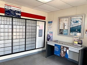 The inside of the new post office shows metal lock boxes on the wall and a desk with brochures. Posters denouncing Identity Theft are on the wall over the desk.