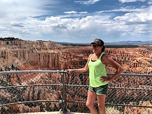 The blog owner, a woman in a bright yellow tank top, olive green shorts, and olive green cap, standing at the fence overlooking Bryce Canyon. Welcome to my blog page!