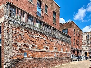 A red-brick building. The side of the building has a very rough finish. There are bricks double-thick in some places, and the bement is oozing out from between the bricks.