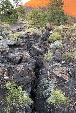 A huge crack in the earth goes from the bottom of the picture, to the top of it, leading up to the red-rock dome of the volcano