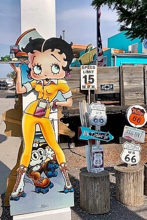 Dressed in yellow, wearing roller skates, holding a tray of food, with a cat on skates between her feet, it's Betty Boop!