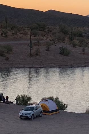 A car and a tent at the edge of a lake.
