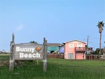 A sign reads Sunny Beach, with colorful houses behind it.