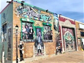 This is the other entire wall (the same building!) of murals: Somebody sitting on the stairs in front of the door, somebody in the window, somebody standing on the corner by a lampost.