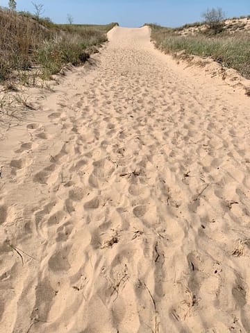 A wide sandy pathway going straight up to where it meets the sky, understanding that the beach is beyond that.