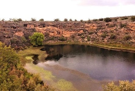 A large pond with a rocky wall behind it. Within the wall are native cave dwellings.