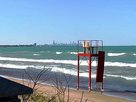 A lifeguard tower in the foreground is displaying a red flag, which means No Swimming. In the background, on the horizon, is the Chicago Skyline.