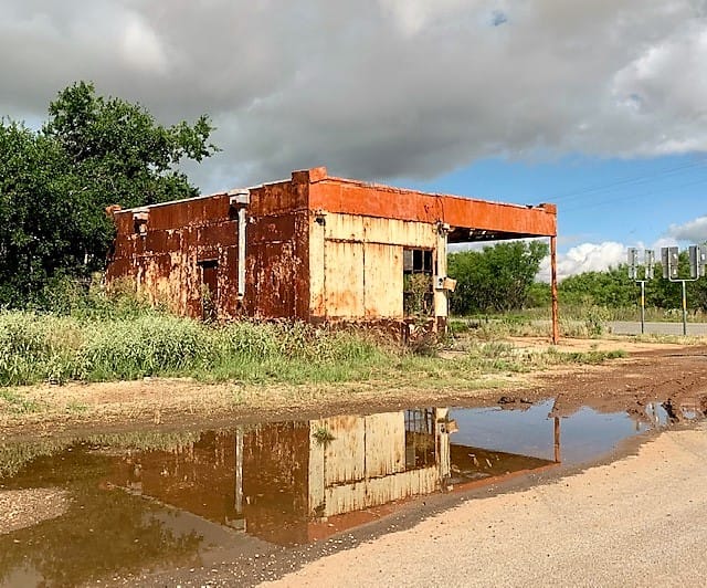 First-ever gas station, and its reflection in a puddle by the road.