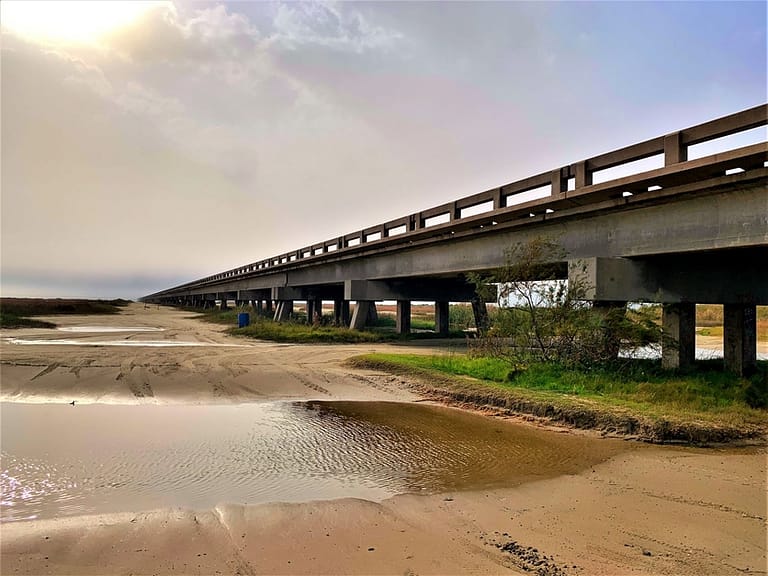 When you drive under the bridge, the terrain is sandy with big dips (holes) that hold water. It's not clear what happens beyond what the eye can see.