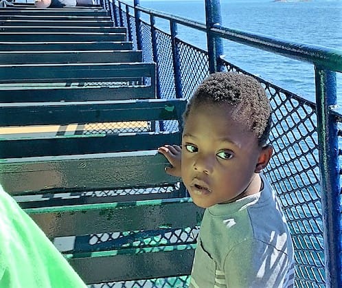 A 5 year old black boy in a sage-green t-shirt next to the lime green sleeve of his mom's shirt, which is reflecting onto him. 