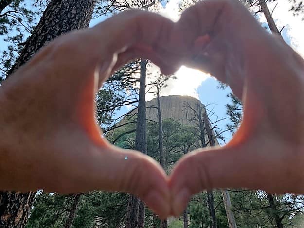 Hands in the shape of a heart with Devils Tower behind