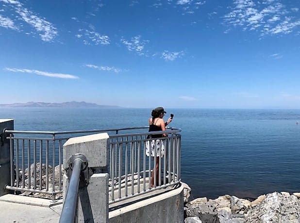 A woman with her back to the camera, stands on a short raised pier (with a railing) Overlooking the Great Salt Lake