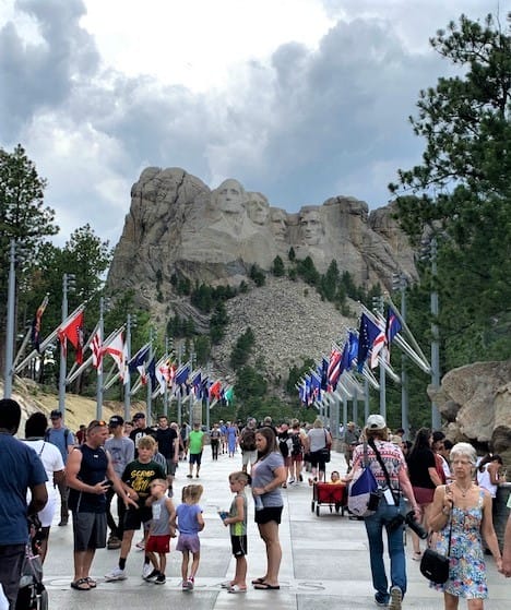 Look down the sidewalk lined with flags. Just raise your chin a little, and there it is! Four Presidential Faces etched into the side of a mountain: George Washington, Thomas Jefferson, Theodore Roosevelt, and Abraham Lincoln. i.e, Mount Rushmore