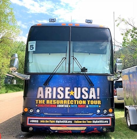 The front of a tour bus reads, "ARISE USA The Resurretion TOur. Constitutional Counties, Faith, Family, Freedom. #UNRIG Join the Fight: BigBatUSA.org"